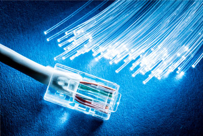 Smiling mom sitting on a couch holds a tablet and explains fiber optic speeds while her daughter sits in her lap and watches
