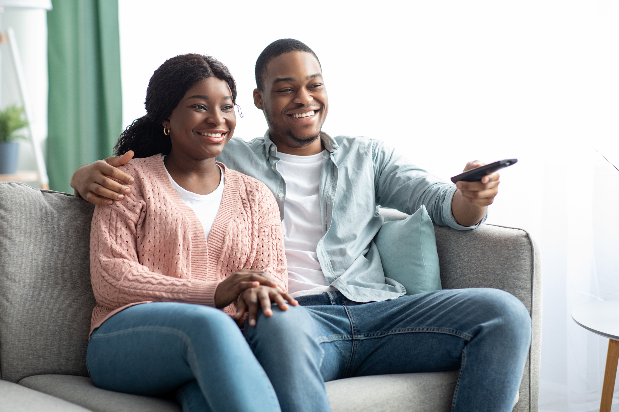 A couple streaming local TV with a remote in the mans hand.